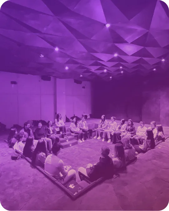A circle of people seated on the floor of a gathering room